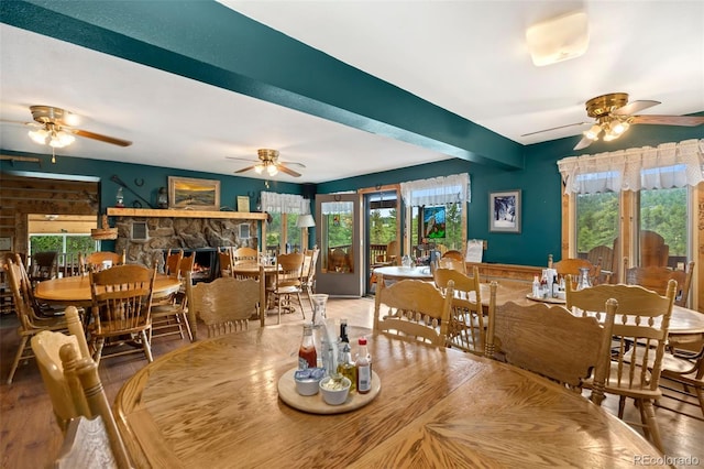 dining room with wood-type flooring, ceiling fan, and a stone fireplace