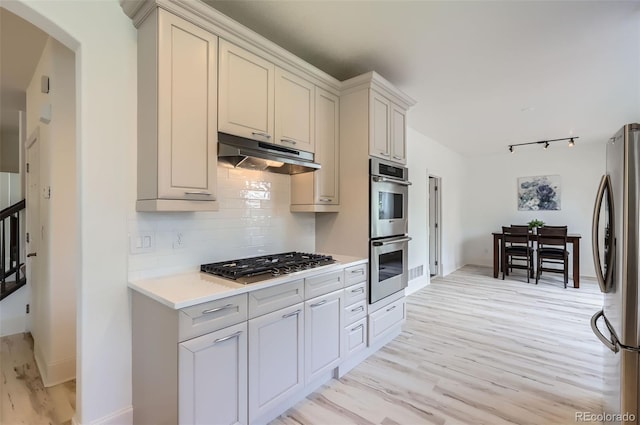 3525 Rinn Valley Dr, Longmont, CO 80504 - kitchen with appliances with stainless steel finishes, under cabinet range hood, light wood-style floors, arched walkways, and decorative backsplash
