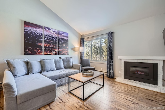 living room with hardwood / wood-style flooring, lofted ceiling, and a brick fireplace