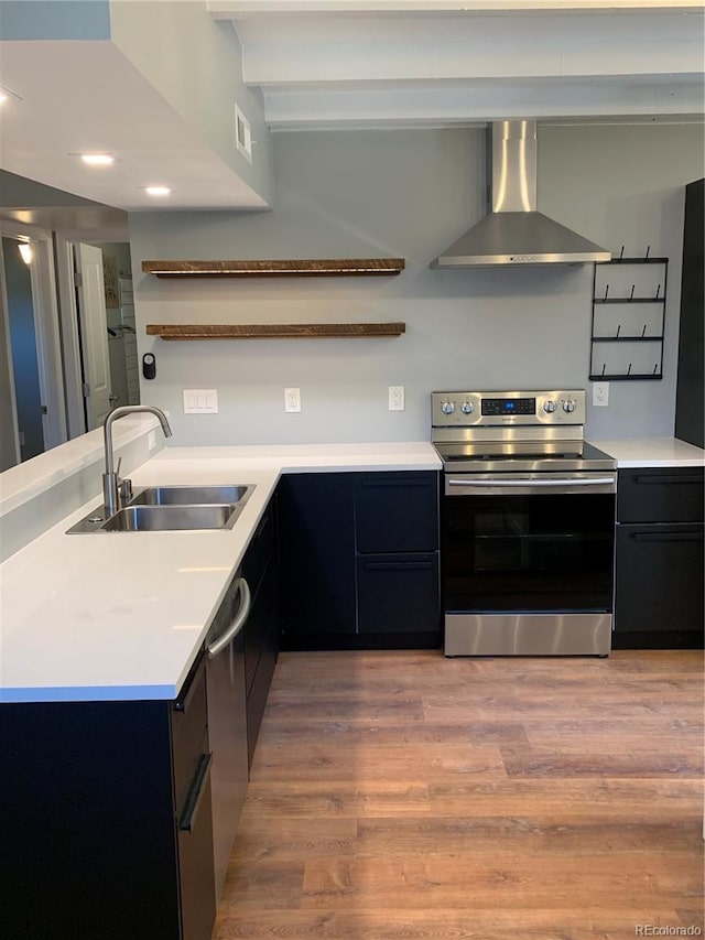 kitchen with a sink, light countertops, appliances with stainless steel finishes, wall chimney range hood, and open shelves