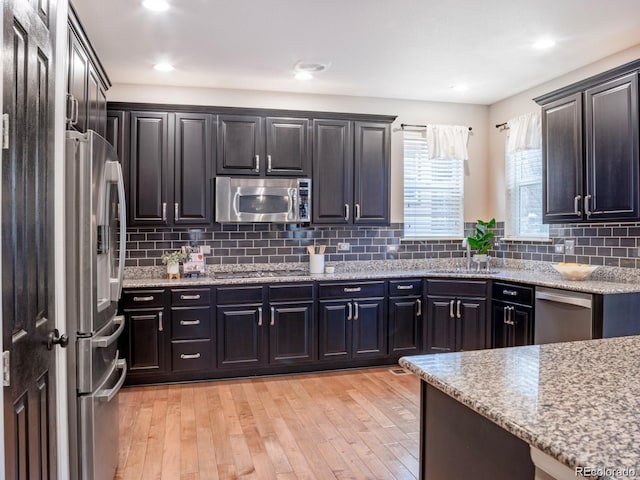 3472 Harvard Pl, Broomfield, CO 80023 - kitchen with appliances with stainless steel finishes, a sink, light wood-style flooring, light stone countertops, and decorative backsplash