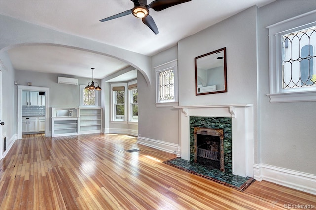 unfurnished living room featuring a wall unit AC, hardwood / wood-style floors, baseboards, and a ceiling fan
