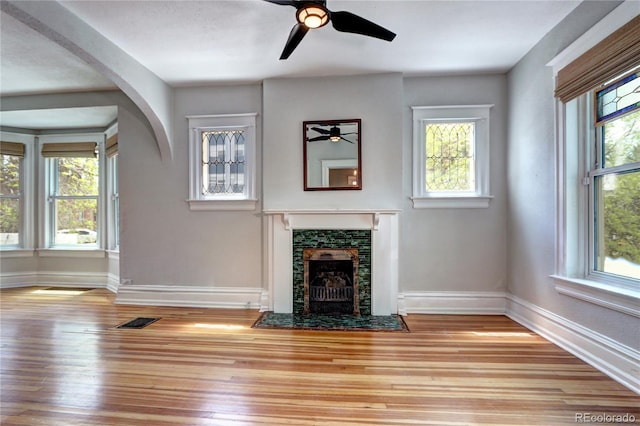 unfurnished living room with ceiling fan, healthy amount of natural light, a fireplace with flush hearth, and baseboards