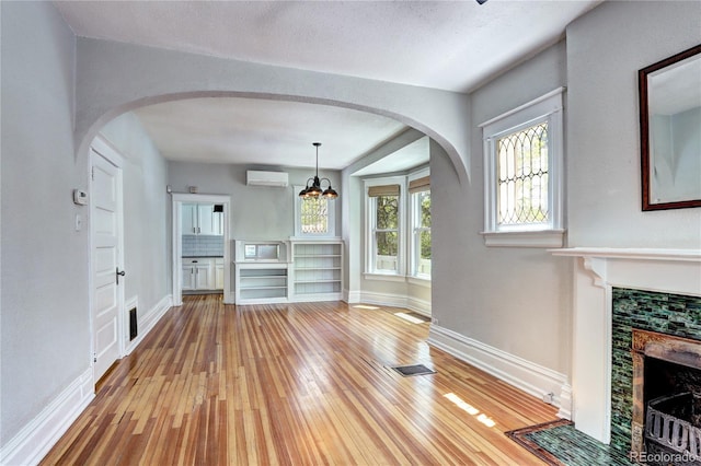 unfurnished dining area with a wall mounted air conditioner, light wood finished floors, a fireplace, and baseboards
