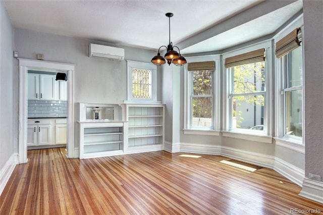 unfurnished dining area featuring a wall mounted air conditioner, light wood-style flooring, and baseboards