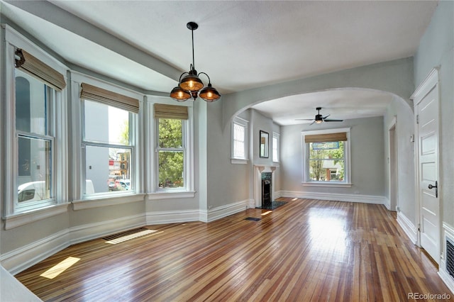 unfurnished living room with arched walkways, wood-type flooring, a fireplace, and baseboards