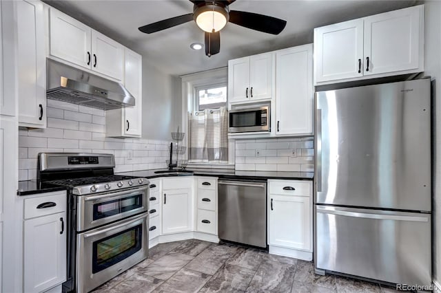 kitchen with stainless steel appliances, under cabinet range hood, a sink, dark countertops, and white cabinetry