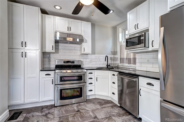 kitchen with stainless steel appliances, under cabinet range hood, a sink, dark countertops, and recessed lighting