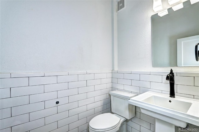 half bathroom with tile walls, toilet, a sink, and wainscoting