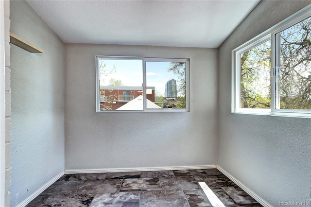 empty room with baseboards, plenty of natural light, a textured wall, and stone finish flooring
