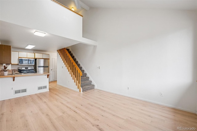 unfurnished living room with stairs, visible vents, high vaulted ceiling, and light wood-style floors
