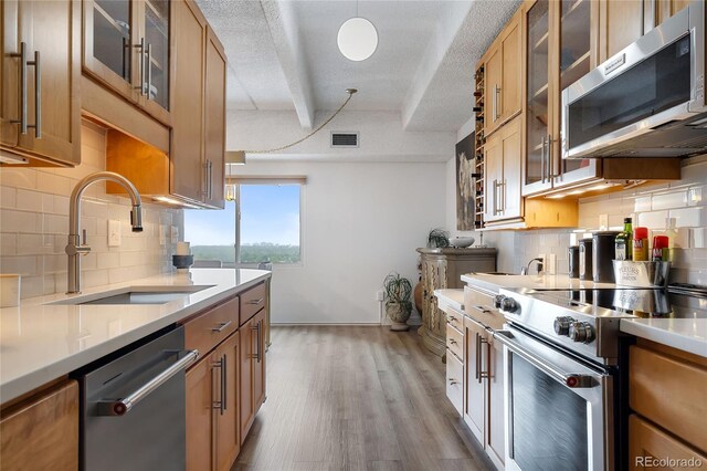 kitchen with stainless steel appliances, backsplash, sink, light wood-type flooring, and a textured ceiling