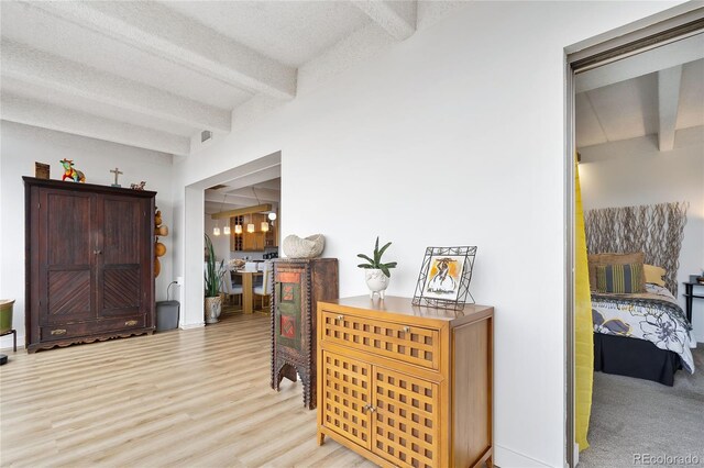 foyer with light hardwood / wood-style floors, beamed ceiling, and a textured ceiling