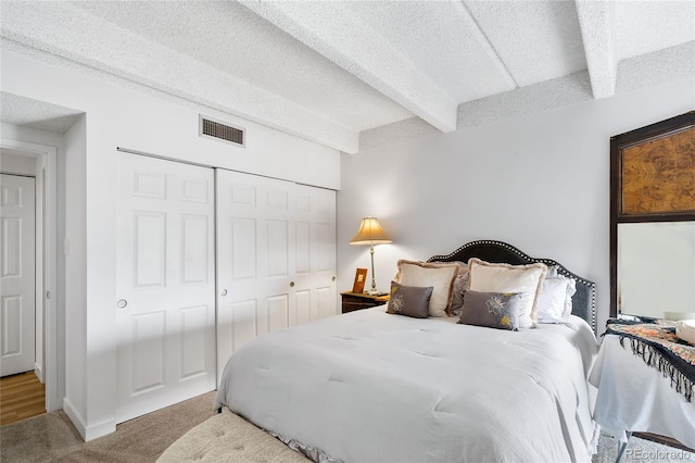 carpeted bedroom with a closet, a textured ceiling, and beamed ceiling