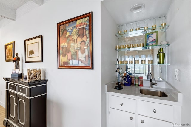 bar with a textured ceiling, sink, and white cabinets