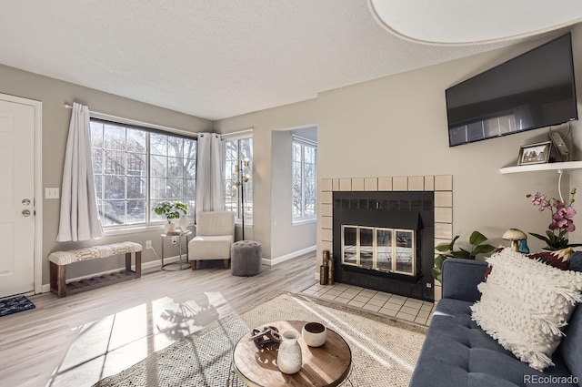 living room with a healthy amount of sunlight, a tiled fireplace, hardwood / wood-style floors, and a textured ceiling