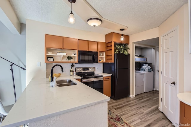 kitchen with pendant lighting, sink, washer and clothes dryer, black appliances, and kitchen peninsula