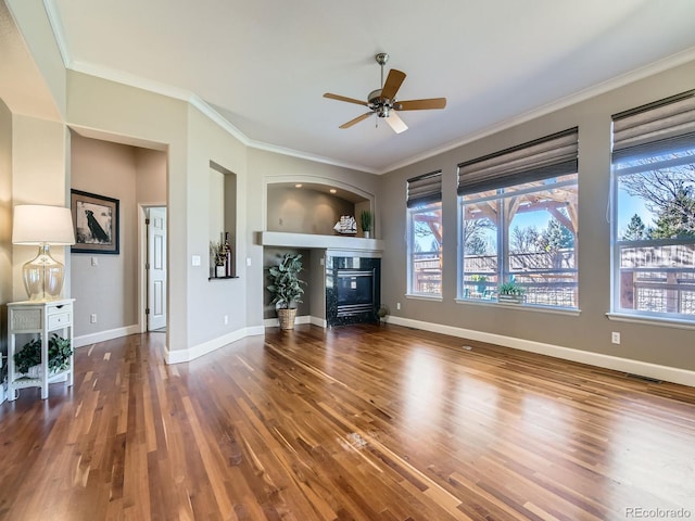 unfurnished living room with wood finished floors, plenty of natural light, a glass covered fireplace, and crown molding