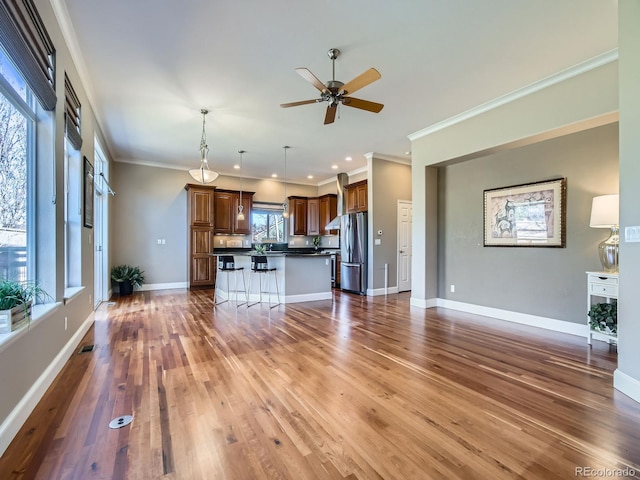 unfurnished living room with crown molding, ceiling fan, wood finished floors, and baseboards