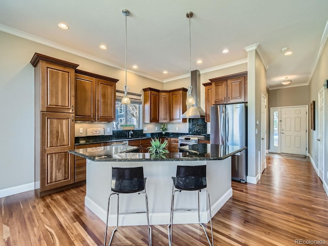 kitchen with a kitchen island, wood finished floors, stainless steel appliances, wall chimney range hood, and a sink