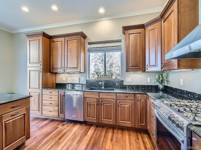 kitchen with wall chimney exhaust hood, ornamental molding, stainless steel appliances, light wood-style floors, and a sink