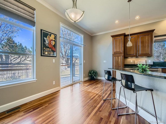 kitchen featuring a breakfast bar area, wood finished floors, visible vents, ornamental molding, and pendant lighting