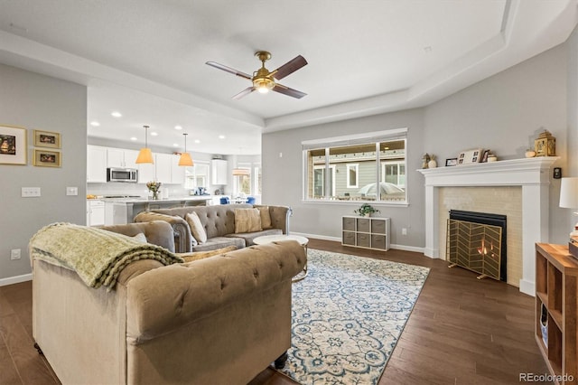 living room with baseboards, dark wood finished floors, a ceiling fan, a tile fireplace, and recessed lighting