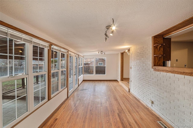 interior space with wood-type flooring, a textured ceiling, and brick wall