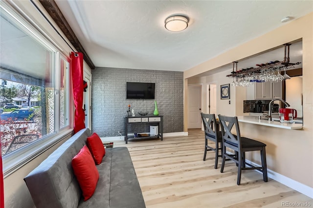 dining space featuring light wood-style flooring, bar area, and baseboards
