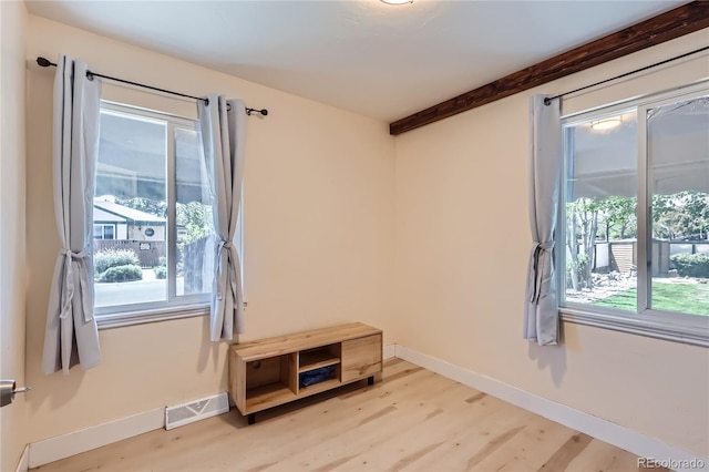 empty room with light wood-style flooring, beam ceiling, and baseboards
