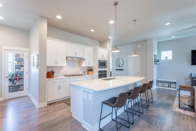21574 E 59th Dr, Aurora, CO 80019 - kitchen with appliances with stainless steel finishes, a sink, under cabinet range hood, wood finished floors, and a center island with sink