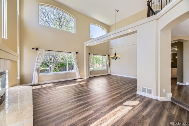 2950 Wyecliff Ln, Highlands Ranch, CO 80126 - unfurnished living room with a towering ceiling, arched walkways, a chandelier, wood finished floors, and baseboards