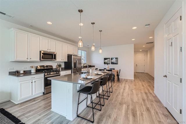 kitchen featuring white cabinets, stainless steel appliances, hanging light fixtures, and a center island with sink