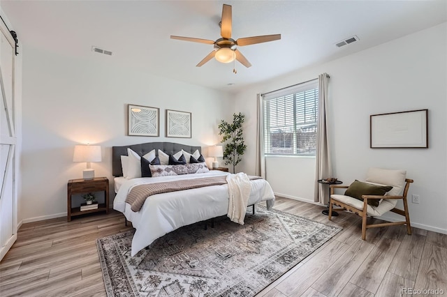 bedroom featuring a barn door, ceiling fan, and light wood-type flooring