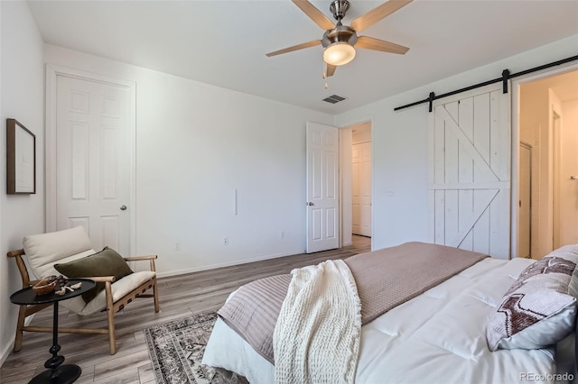 bedroom featuring hardwood / wood-style floors, a barn door, and ceiling fan