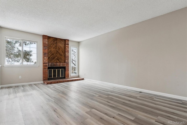 unfurnished living room with light hardwood / wood-style flooring, a textured ceiling, and a brick fireplace