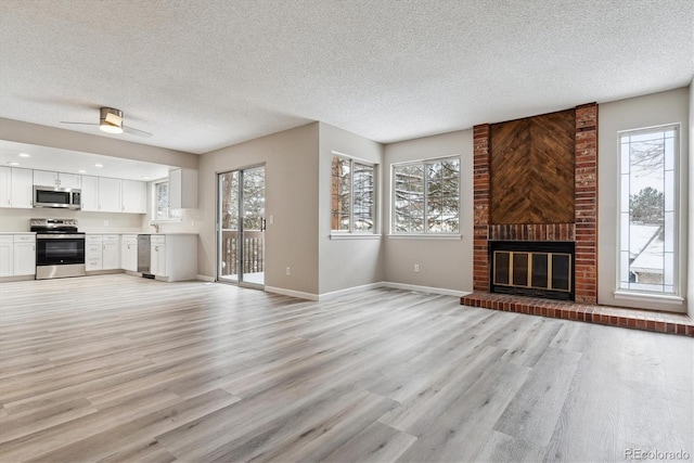 unfurnished living room with ceiling fan, light wood-type flooring, a textured ceiling, and a brick fireplace