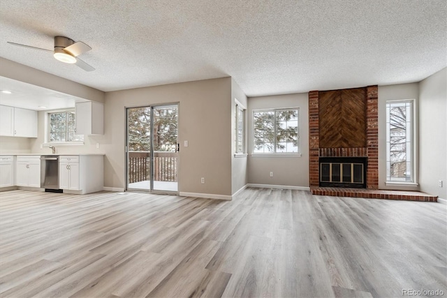 unfurnished living room featuring ceiling fan, light hardwood / wood-style floors, a textured ceiling, and a brick fireplace