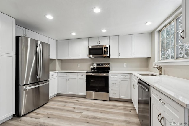 kitchen featuring light stone countertops, light wood-type flooring, stainless steel appliances, sink, and white cabinets