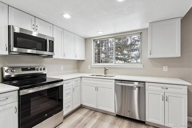 kitchen with sink, light hardwood / wood-style flooring, white cabinets, and appliances with stainless steel finishes