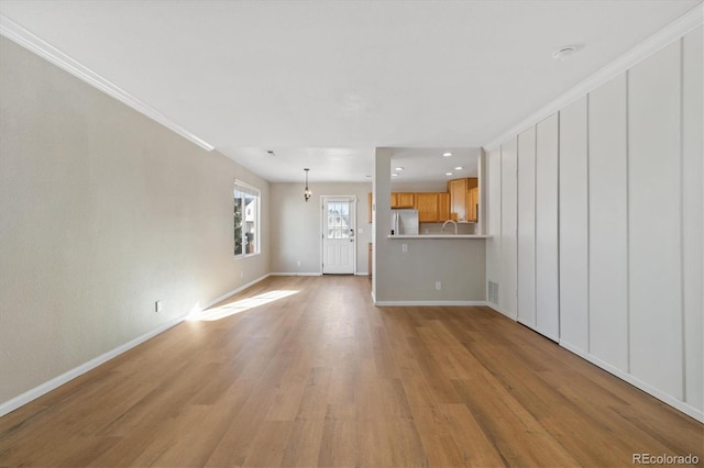 unfurnished living room featuring sink, light wood-type flooring, and crown molding