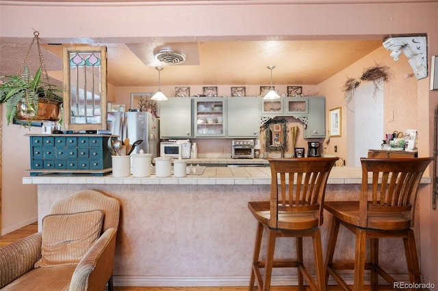 715 Main St, Georgetown, CO 80444 - kitchen featuring freestanding refrigerator, tile countertops, white microwave, glass insert cabinets, and a kitchen breakfast bar