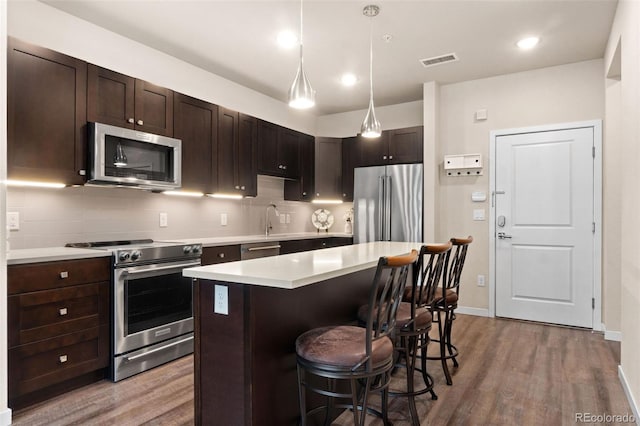 kitchen with appliances with stainless steel finishes, pendant lighting, a breakfast bar, a kitchen island, and hardwood / wood-style flooring