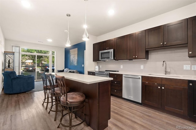 kitchen featuring pendant lighting, sink, light hardwood / wood-style flooring, a kitchen bar, and stainless steel appliances