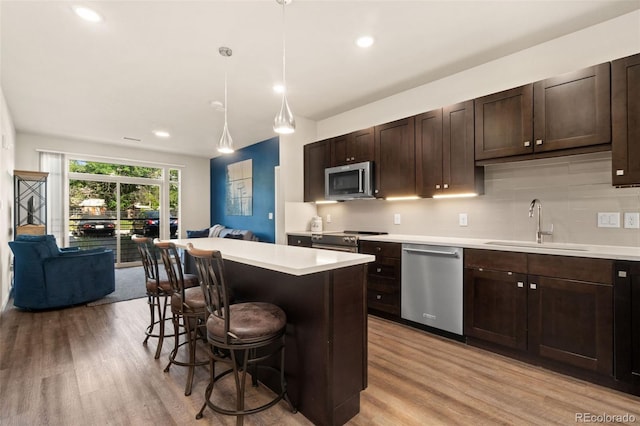 kitchen featuring pendant lighting, a breakfast bar, backsplash, appliances with stainless steel finishes, and light hardwood / wood-style floors