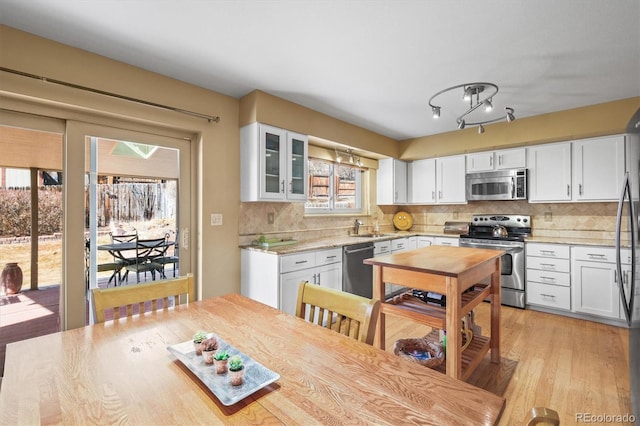 kitchen with glass insert cabinets, white cabinetry, stainless steel appliances, and backsplash