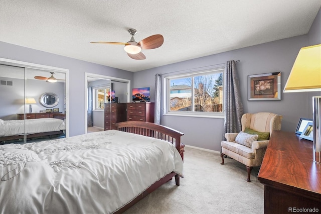 bedroom featuring multiple closets, visible vents, a ceiling fan, carpet flooring, and a textured ceiling