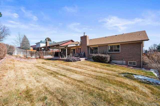 back of property featuring a yard, brick siding, fence, and a chimney