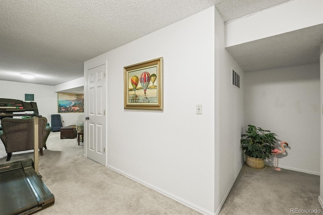 hallway with baseboards, visible vents, a textured ceiling, and light colored carpet