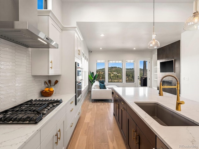 kitchen with tasteful backsplash, wall chimney range hood, sink, white cabinets, and light hardwood / wood-style flooring